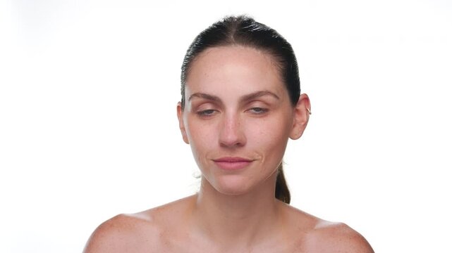 Close up of fair-skinned freckled Latin woman with blue eyes and ponytale hairstyle lifts gaze to the camera on white background | skin moisturizing concept