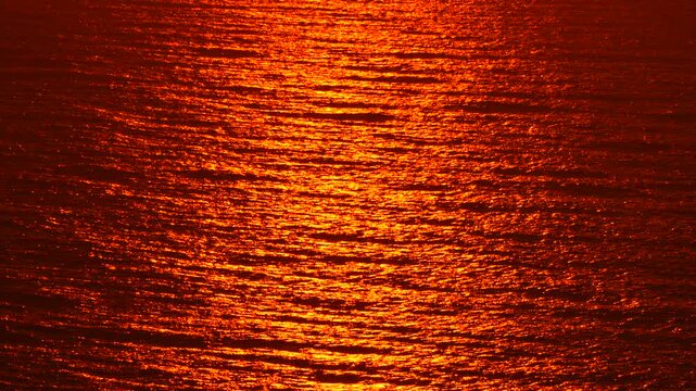 Water, sunset, reflection shimmers on the ocean waves creating a deep red and orange abstract background pattern at dusk.