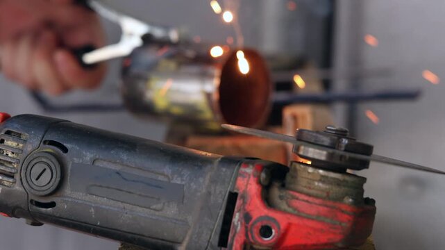 Angle grinder machine in foreground with welder fabricator joining steel tubes out of focus