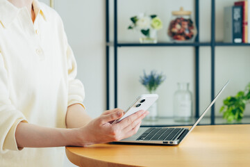 家でスマホを持ってパソコンを使う若い女性の手元 © pain au chocolat