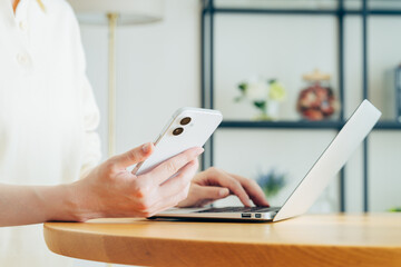 家でスマホを持ってパソコンを使う若い女性の手元 © pain au chocolat