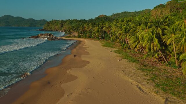 Aerial Forward Tracking Shot Along Duli Beach Shoreline in El Nido, Philippines. Drone View of Sweeping Golden Sand, Rolling Ocean Surf, and Tropical Jungle.