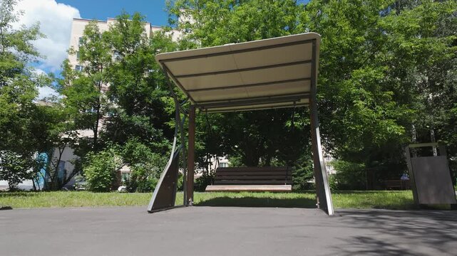 Empty playground swing gently swinging in sunny residential park