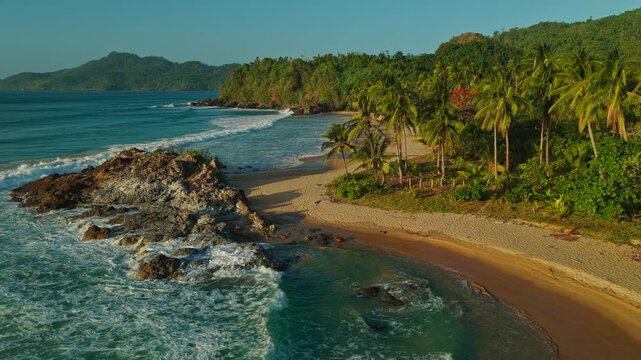 Aerial Orbit Around Rocky Point at Duli Beach in El Nido, Philippines. Cinematic Drone Right to Left Curved Tracking View of Rugged Rocks, Golden Sand, and Ocean Surf.