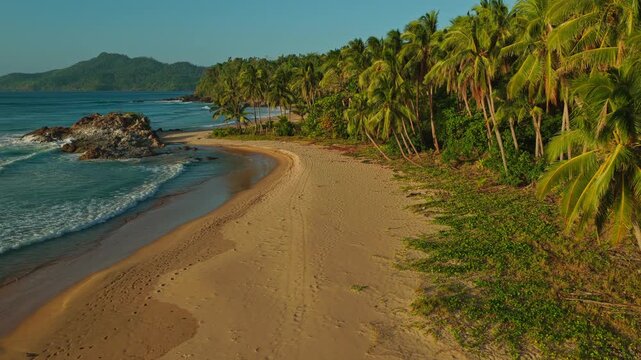 Aerial Backwards Reveal of Duli Beach in El Nido, Philippines. Cinematic Drone Pull Away Over Sweeping Golden Sand Shoreline, Ocean Surf, and Tropical Jungle.