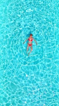 Top down view of a woman in pink swimsuit swimming on her back in the pool.