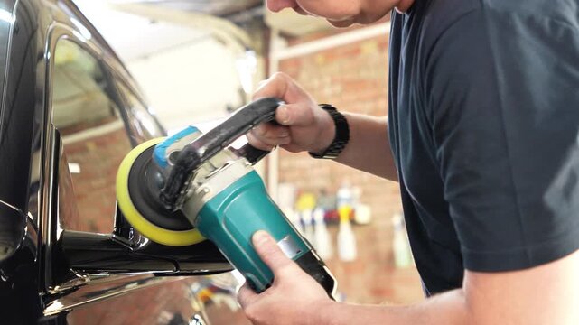A car service worker polishes the car body with a polishing machine. Detailing and polishing of the car. Car detailing - hands with an orbital polishing machine in an auto repair shop. Detailing car. 