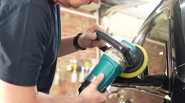 A car service worker polishes the car body with a polishing machine. Detailing and polishing of the car. Car detailing - hands with an orbital polishing machine in an auto repair shop. Detailing car. 