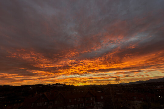 Dramatic sunset sky with vibrant orange clouds and dark moody textures over a subtle town silhouette creating a powerful natural background concept