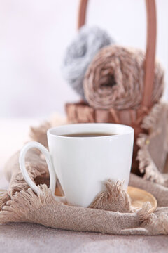 Cup of coffee stands against a background of balls of yarn. Beige wool yarn is out of focus. Skeins of yarn are in the basket. Hobby concept