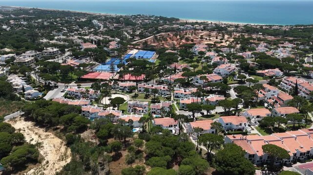 Aerial overview of Quinta do Lago resort buildings in Vale de Lobo, Algarve, Portugal, Europe. Shot of rooftops of luxury cottages in green landscape with mountains on background. Golf fields.