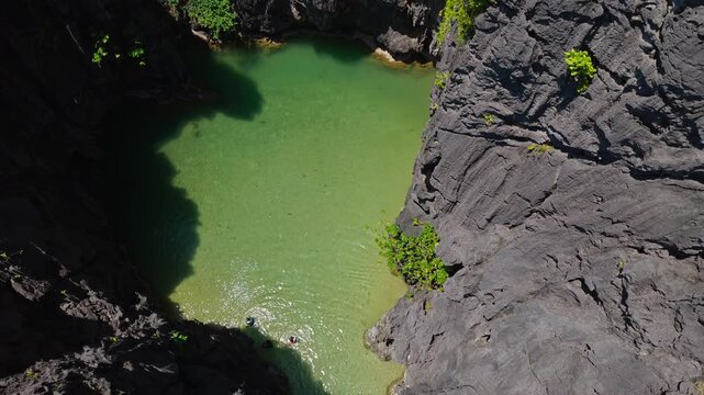 Drone Top Down Reveal of Secret Lagoon in El Nido, Philippines. Aerial Pull Away Shot of Tourists Swimming in Turquoise Water Enclosed by Dramatic Karst Limestone Cliffs.