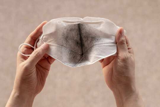 Hands holding dirty white face mask with black dust stain, pollution environment issue problem