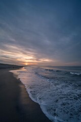 Fototapeta premium Sunset waves along a quiet sandy beach under a dramatic cloudy sky