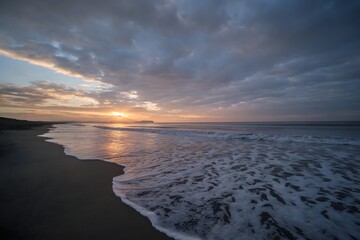 Obraz premium Dramatic Sunset on a Quiet Sandy Beach with Rolling Waves