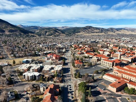 Boulder, Colorado, USA - 26 December 2025: Aerial view of the Flatirons and the city of Boulder, featuring terracotta-roofed buildings, urban streets, and a clear blue sky.