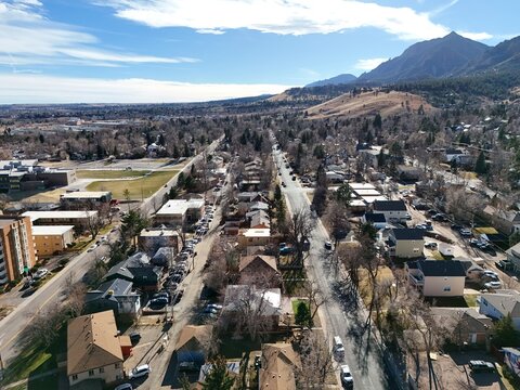 Boulder, USA - 26 December 2025: Aerial view of the Flatirons mountain range rising above residential neighborhoods and streets under a clear blue sky.