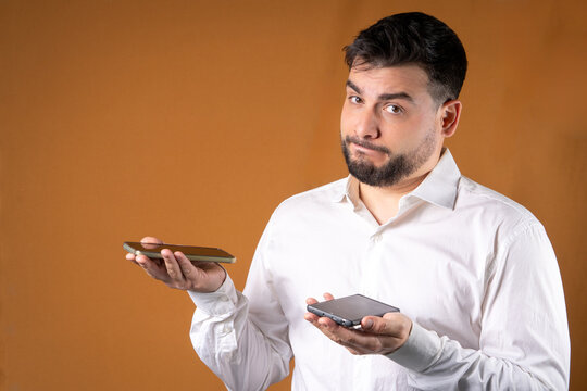 Hombre dudando acerca de que tel&eacute;fono escoger. Hombre con dos telefonos en sus manos con expresi&oacute;n de duda.