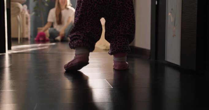 Baby girl making first independent steps on wooden floor. Home lifestyle scene about growing up and mobility