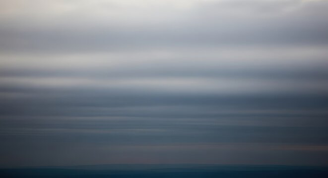 A thick, gray layer of stratus clouds completely dominates the upper atmosphere during a cold afternoon, signifying heavy, diffused light, horizon, textured, monotone