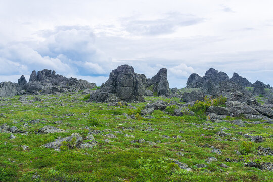 Mountain landscape with green grass and rocks under cloudy sky in summer