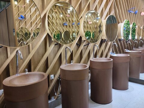 Modern public restroom interior featuring a row of unique cylindrical brown terracotta sinks with elegant chrome faucets and round mirrors mounted on a contemporary wooden slat wall.