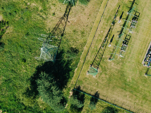 Aerial view of high-voltage power lines and metal pylons standing in a grassy field with shadows cast on the ground in Garkalne, Adazi Municipality, Latvia.