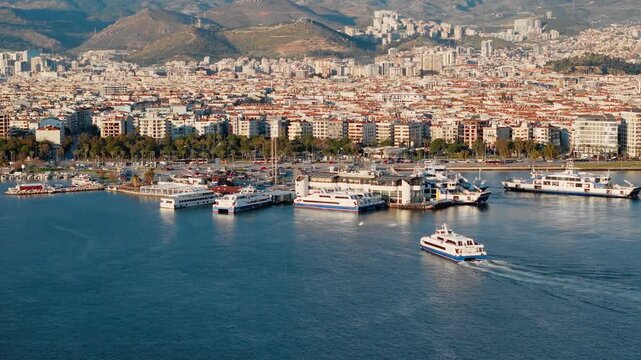 Passenger ferry approaching ferry terminal near waterfront district. Aerial view of urban coastal transport and cityscape