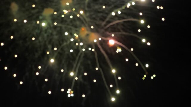 Sparkling fireworks bursts glow in black night sky on holiday blurry view. Exploding fireworks display with floating traces in inky sky at show. Fireworks performance in dark night on holiday event