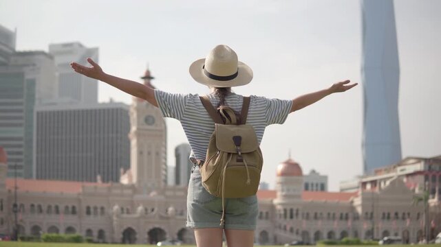 Female tourist in hat with backpack is raising her arms