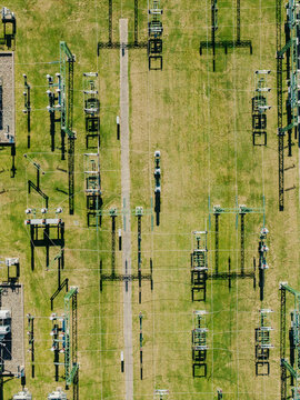 Aerial view of an electrical substation with high-voltage power lines, metal towers, and electrical equipment set against a green grassy field in Garkalne, Adazi Municipality, Latvia.