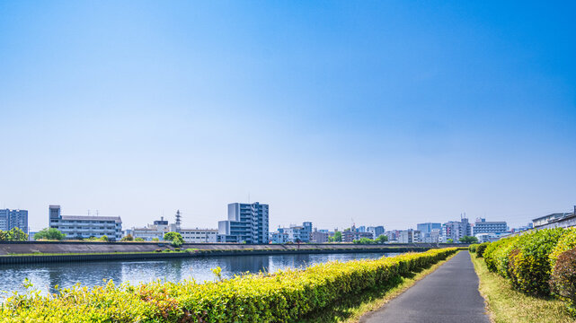 青空の下に続く川沿いのサイクリングロードと都市風景