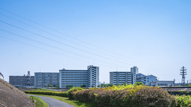 青空と電線が交差する川沿いの高層マンション群