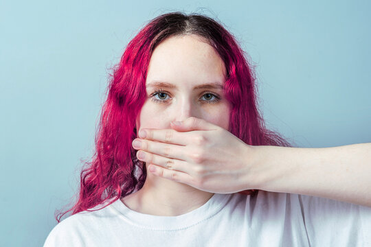 Young woman covering her mouth as a symbol of forced silence, social pressure and fear to speak the truth. Concept of censorship, intimidation, abuse of power and silencing victims.