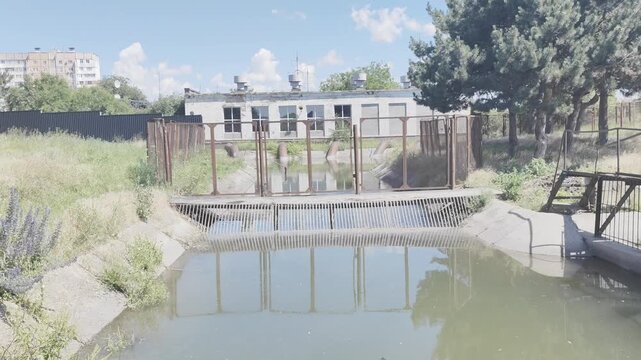 Abandoned industrial water channel with rusty metal gate and old building reflecting in still water outdoors.
Описание: Abandoned industrial water channel with rusty metal gate and old building reflec