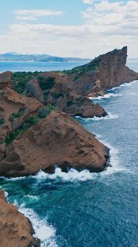 Rocky Mediterranean shoreline with steep cliffs and visible wave action along the base of the rocks. Aerial coastal landscape