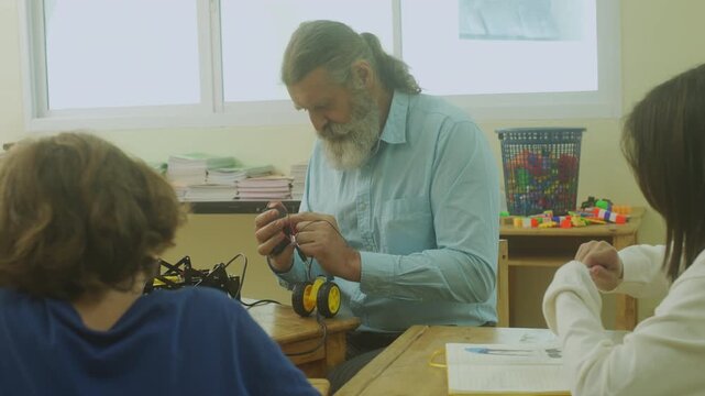 Multi-ethnic elementary school children assembling DIY robotic models during a STEM class with a senior teacher.