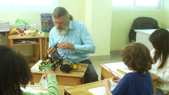 Multi-ethnic elementary school children assembling DIY robotic models during a STEM class with a senior teacher.