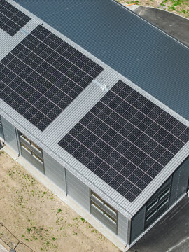 Aerial view of a modern industrial building roof covered with large solar panel arrays, featuring metallic corrugated roofing and clean lines in Riga, Latvia.