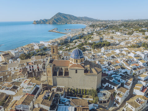 Aerial view of the iconic blue-domed Parroquia de Nuestra Senora del Consuelo overlooking the white rooftops and the Mediterranean coastline in Altea, Valencian Community, Spain.