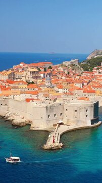 Small boat sailing in front of Dubrovnik Old Harbor and historic city walls on the Adriatic coast.