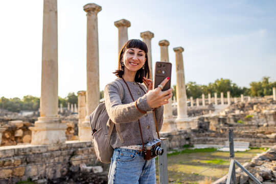 A young woman takes a smartphone selfie against the backdrop of columns and an archaeological site. She creates content for social media. Traveling in Israel, Beit She'an.