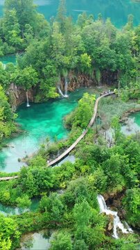 People crossing a wooden boardwalk above beautiful waterfalls in Plitvice Lakes National Park, Croatia.