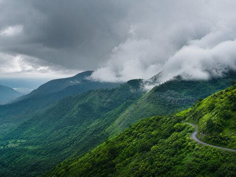 Monsoon clouds rolling over layered green hills with a winding road partly visible