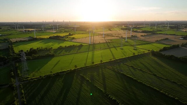 Aerial footage of wind farm and high voltage power lines and electricity transmission infrastructure by sunset.