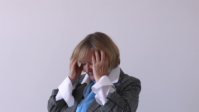 Senior Businesswoman Suffering from Headache. Senior woman holding her temples with eyes closed. Mature woman experiencing headache, stress or fatigue against a plain background.