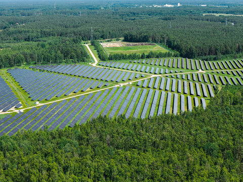 Aerial view of a large solar farm with rows of photovoltaic panels surrounded by dense green forest in Riga, Latvia.