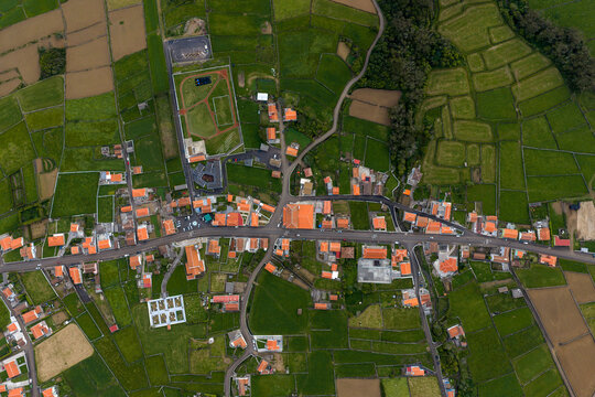Aerial view of the village of Doze Ribeiras with its characteristic orange-tiled rooftops surrounded by lush green agricultural fields and stone walls in Doze Ribeiras, Azores, Portugal.