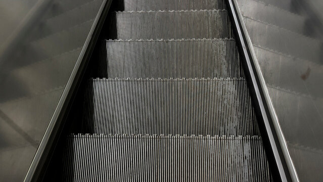 High angle perspective view of an empty moving metal escalator with reflections on glass side panels
