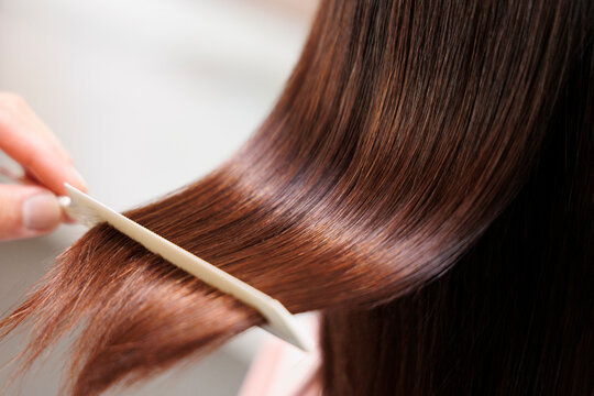 つやのある女性の茶色いロングヘアをコームですく 美髪 ヘアケア トリートメントのイメージ